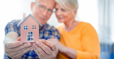 Senioren stel houdt een model huisje vast